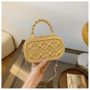 Detalle de bolso de fiesta dorado con texturas de corazón en relieve y asa de metal trenzada