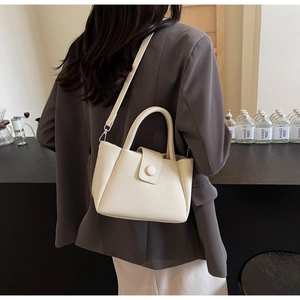 Détail d'un sac bandoulière beige en cuir grainé porté par un mannequin dans un café chic