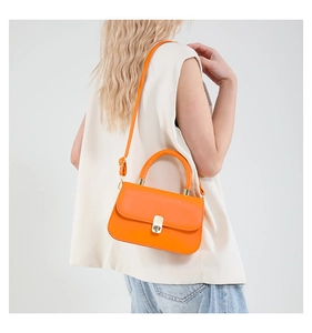 Detail of bright orange textured baguette bag with gold twist lock and top handle