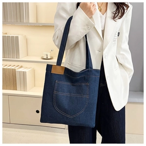 Detail of dark blue denim tote bag with front pocket and brown leather trim on white suit