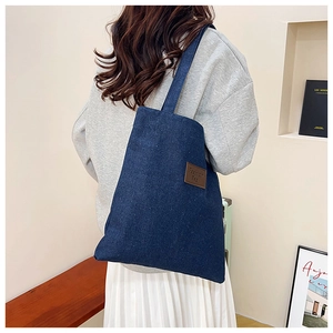 Close-up of durable dark blue denim tote bag with a brown leather logo patch detail