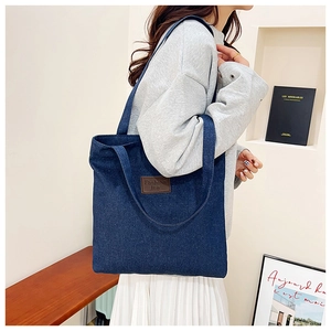 Side view of a large navy denim tote bag with leather tag on a model in a minimal setting