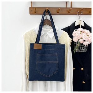 Close-up of a blue denim tote bag with orange stitching and leather patch on a wooden hanger