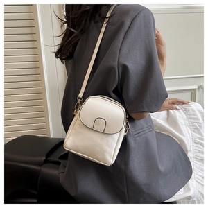 Detailed view of cream-white mini crossbody bag with gold hardware on a gray blazer model