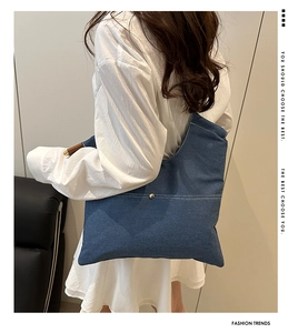 Detailed view of blue denim tote bag with wooden handle and metal buckle on model