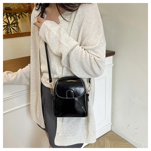 Close-up of black crossbody phone bag in glossy patent leather with gold hardware
