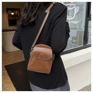 Detail of a brown vintage phone bag with gold hardware worn by a model in a cafe