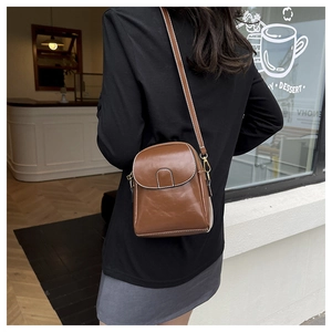 Detail of a brown crossbody phone bag with contrast stitching and glossy finish