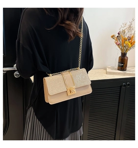 Detail of beige shoulder bag with sparkling gold sequins and metal chain strap on model