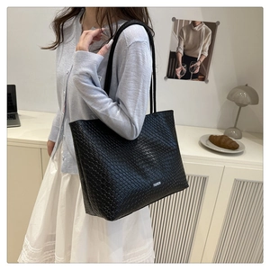 Close-up of black woven texture tote bag with a white fashion label and slim shoulder straps