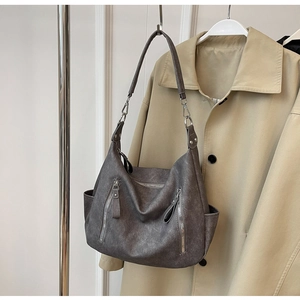 Detail van donkergrijze halve maan tas met ritszakken tegen een klassieke trenchcoat achtergrond