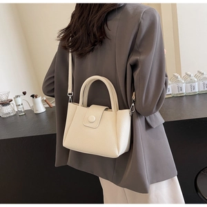 Detail of a creamy white pebbled leather handbag featuring rounded handles and a flap closure