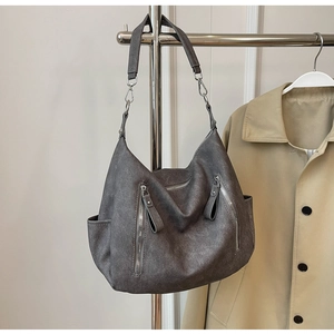 Detail van vintage grijze hobo-tas met zilveren ritsen hangend voor een trenchcoat