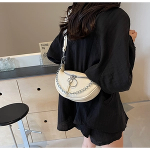 Detail of creamy white crescent saddle bag with silver chain strap on a model shoulder