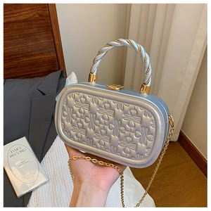 Detalle de bolso rígido plateado metalizado con texturas y asa trenzada bicolor