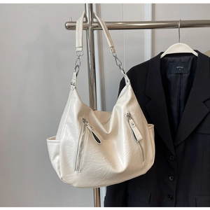 Detail van beige halve maan tas met geplooid leer en metalen ritszakken aan voorkant