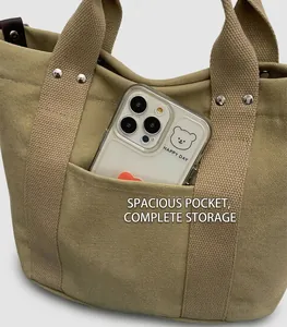 Dettaglio della capiente tasca frontale della borsa tote in tela kaki con smartphone