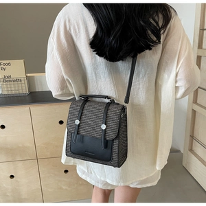 Close-up of retro woven shoulder bag with leather flap shown on model in warm interior