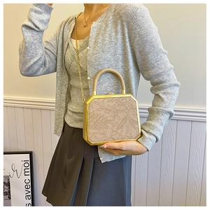 Detail of apricot octagonal box bag with floral relief and gold chain strap worn by model