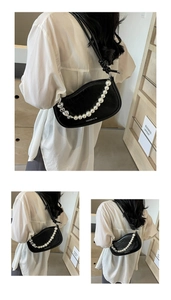 Detail of black leather underarm bag featuring pearl chain and silver heart charm