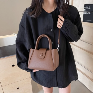 Sac à main marron en cuir grainé avec poignée et bandoulière porté par un mannequin