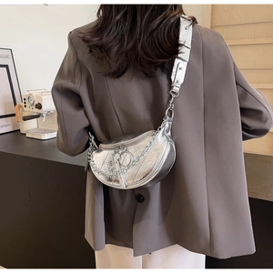 Detail of silver metallic dumpling bag with chain strap worn by model in urban setting