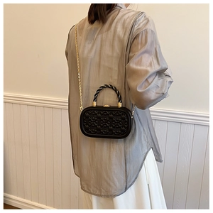 Detalle de mini bolso caja negro acolchado con cadena dorada llevado por una modelo