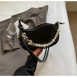 Detail of black crescent shoulder bag with silver heart charm and pearl chain accent