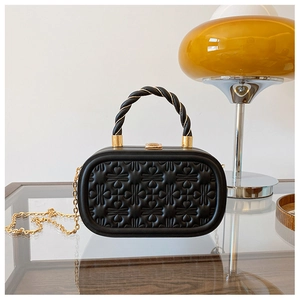 Detalle de bolso caja negro con corazones grabados y asa dorada trenzada