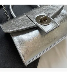 Detail shot of silver metallic crossbody bag featuring pleated texture and round twist lock