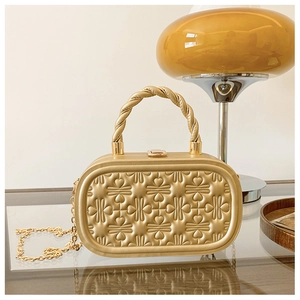 Detalle de bolso tipo caja dorado con patrones de corazones 3D y asa trenzada