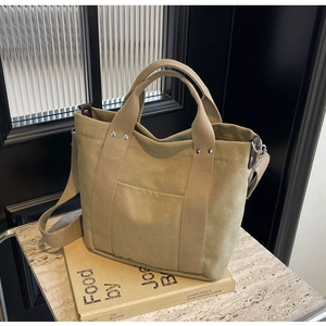 Dettaglio della borsa tote in tela kaki con finiture in pelle e rivetti su un libro
