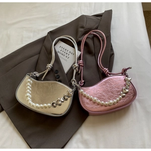 Detail of metallic underarm bags with heart charms and faux pearl chains on fabric