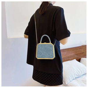 Detail of light blue box bag with embossed floral texture and gold metal frame chain
