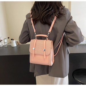 Close-up of pink mini straw woven backpack with silver hardware on a gray suit model