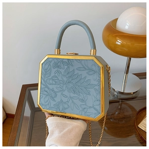 Detail of light blue box bag featuring floral embossing and gold metal trim