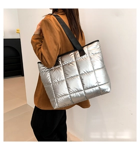 Detalle del bolso tote acolchado plateado con acabado metálico y correa de hombro negra