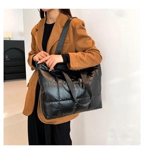 Detalle de un bolso tote acolchado negro grande con acabado brillante y correa ancha