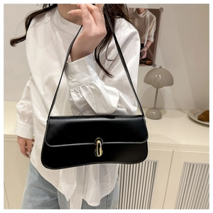 Close-up of a minimalist black baguette bag with gold metal buckle and sleek faux leather