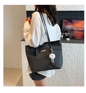 Detail of black woven texture tote bag with golden logo plate and white furry monster charm