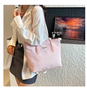 Detailed view of pink woven tote bag with metallic logo plate and slim leather straps