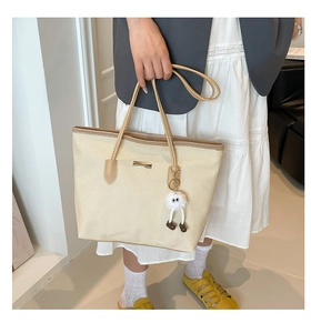 Détail du grand sac cabas tissé avec bordure en cuir et charm peluche porté par mannequin