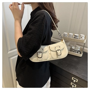 Detail of cream shoulder bag with double front pockets and retro metal buckles on a model