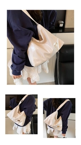 Detail view of large white patent leather tote bag with gold metal buckle and wide strap
