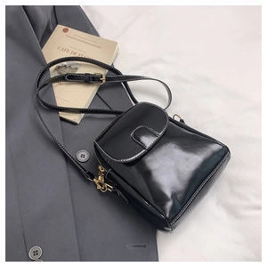 Detail view of black patent leather crossbody bag with white stitching and gold hardware