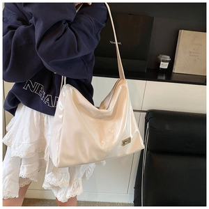 Detailed side view of cream white patent leather tote bag with metal logo and zipper closure