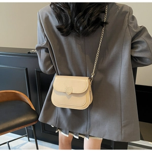Detail of crossbody bag with golden heart buckle and fine stitching in a minimalist setting