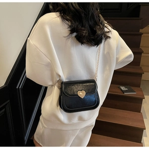 Close-up of black leather saddle bag with gold heart-shaped buckle and chain strap