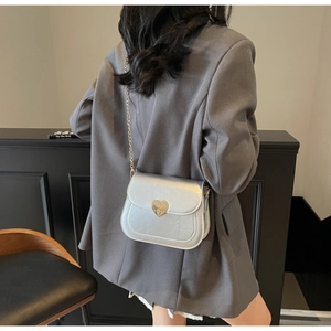 Detailed view of a silver square bag with a heart metal buckle and fine gold chain strap
