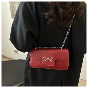 Close-up of a red leather crossbody bag featuring a silver metal bow buckle and chain strap